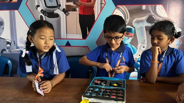 Three students look over an electronics kit in a robotics-themed classroom