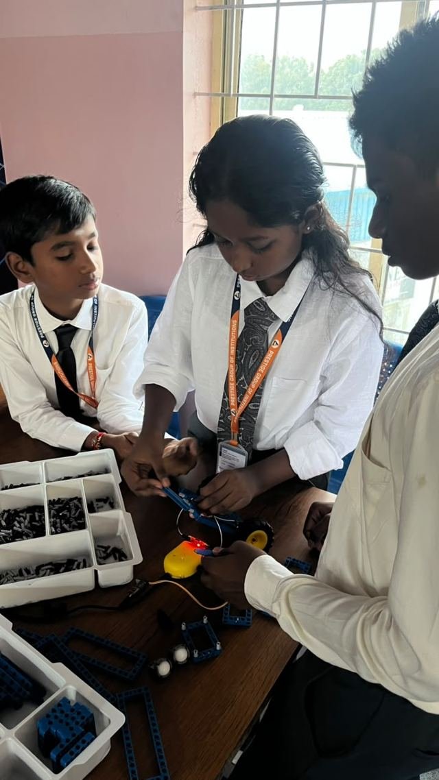 Students assemble a wheeled robot from a construction kit at a classroom table