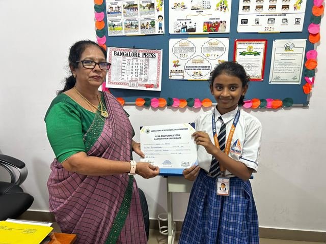 A teacher presents a certificate to a student in front of a classroom notice board
